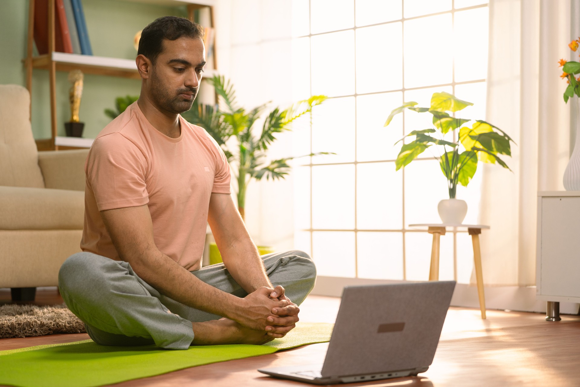 Indian man doing exercise by watching yoga video tutorial or online class from laptop at home - concept of virtual fitness training, stretching workout and Digital Wellness